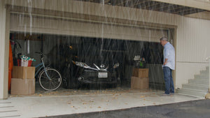 Man standing outside of a garage with rainfall and debris pouring into the garage making it dirty and wet